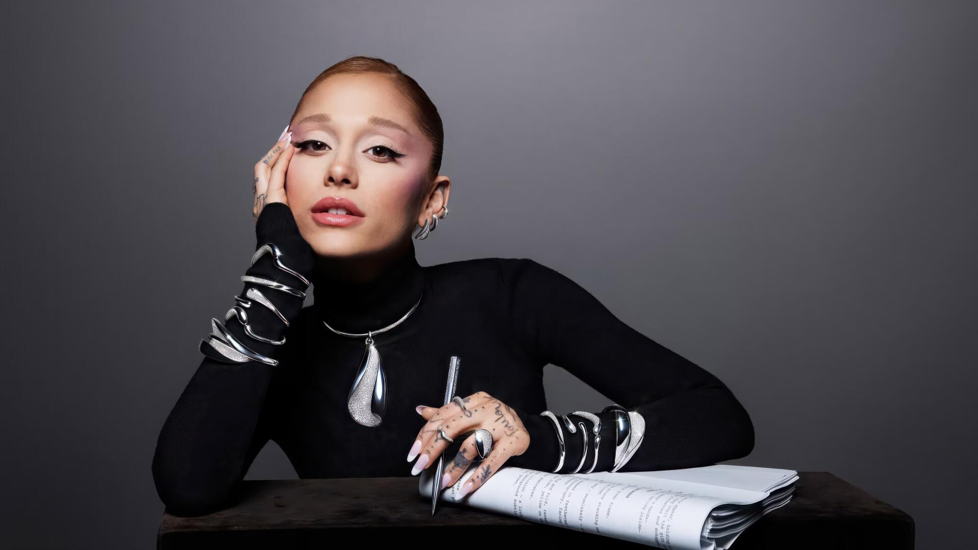 Stylish female pop singer in black turtleneck, bold makeup and statement jewelry, posing with a notebook; 2K Quad HD PC desktop wallpaper evoking music and studio vibes.