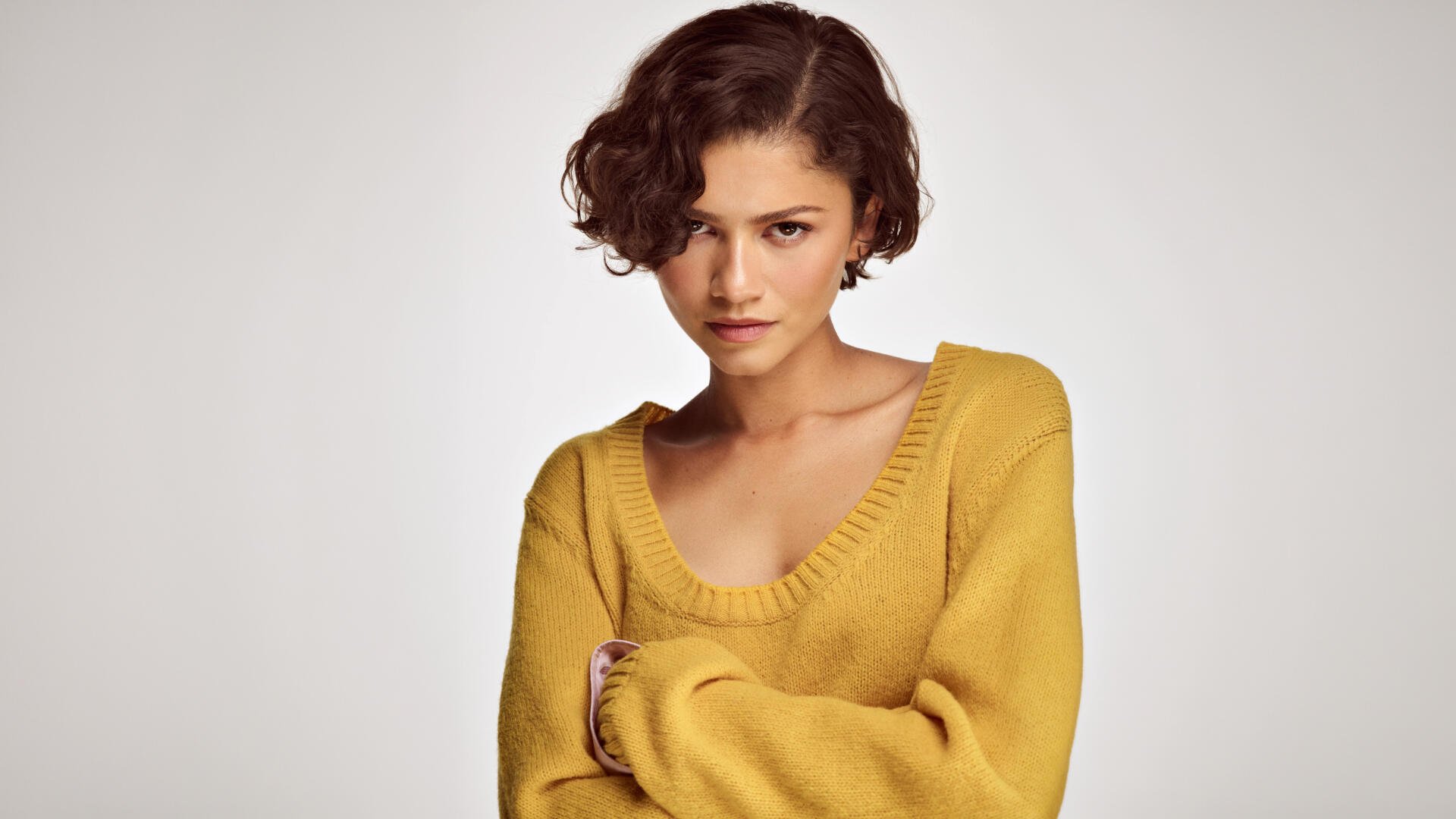 Close-up portrait of a young woman with short curly hair wearing a mustard sweater against a neutral backdrop — 5K Ultra HD PC desktop wallpaper/background.