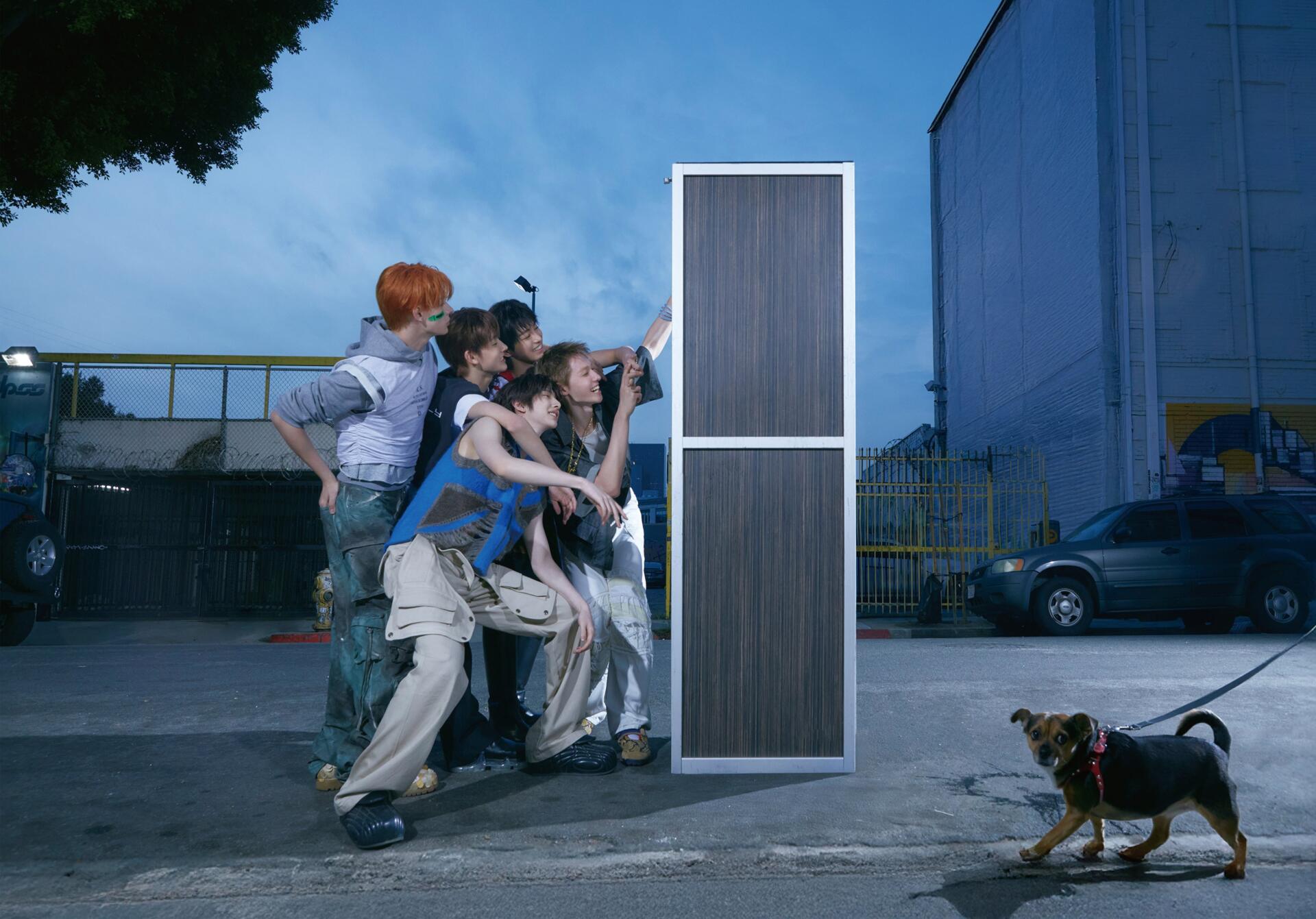 Cortis Color Outside the Lines 4K Ultra HD PC desktop background: a group of people push a tall freestanding door in an industrial lot at dusk while a small dog tugs on its leash.