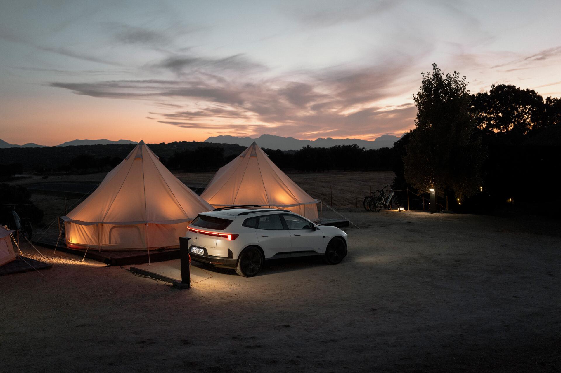 Polestar 4 SUV beside glowing glamping tents at sunset, 8K Ultra HD PC desktop wallpaper and background.