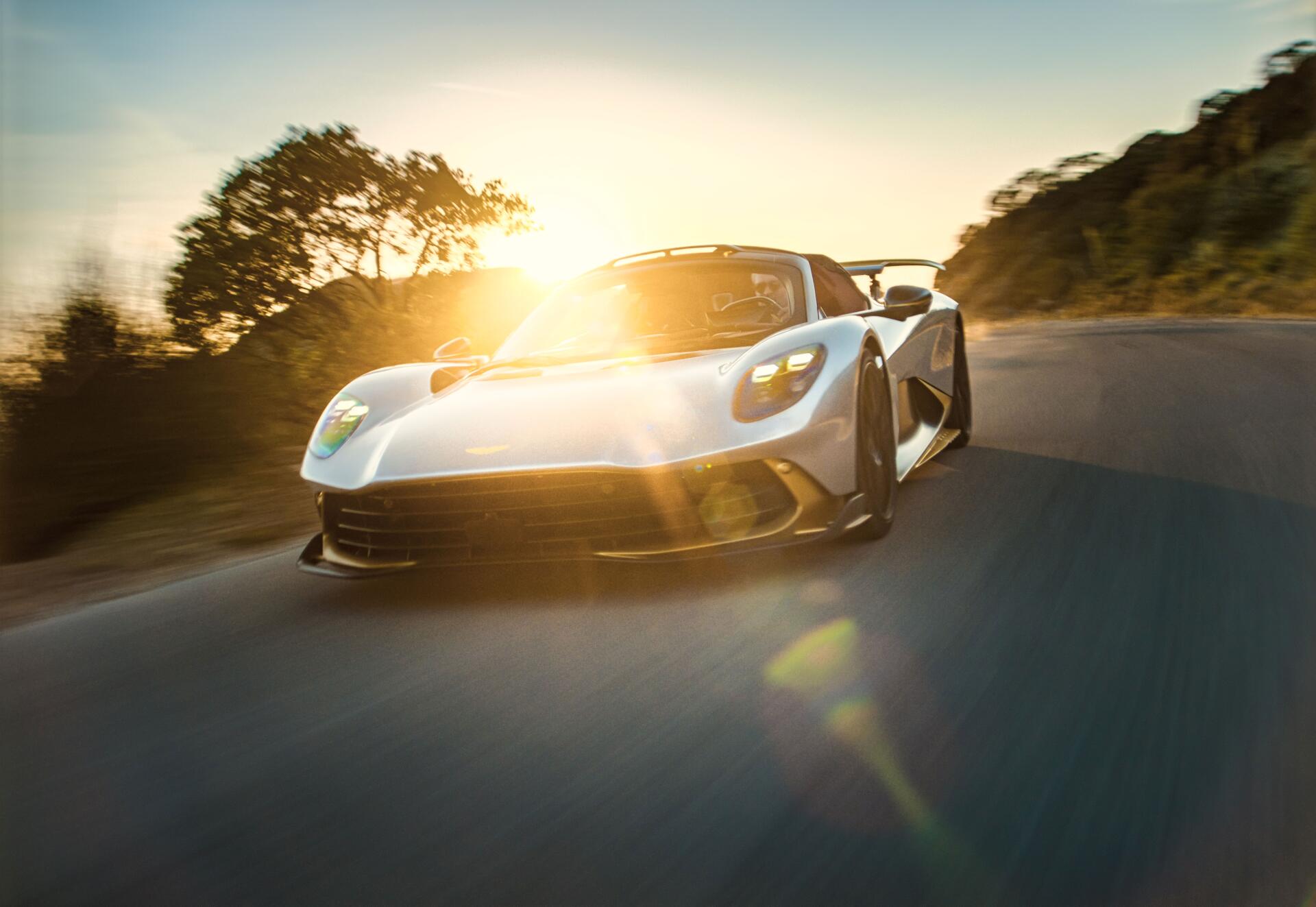 Aston Martin Valhalla Spider sports car speeding along a sunlit road in an 8K Ultra HD PC desktop wallpaper.