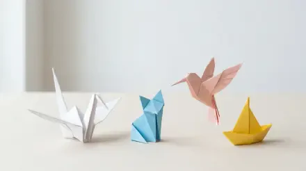 Clean 5K Ultra HD PC desktop wallpaper and background showing a minimal beige surface with four origami figures: white crane, blue folded animal, pink hummingbird, yellow paper boat.