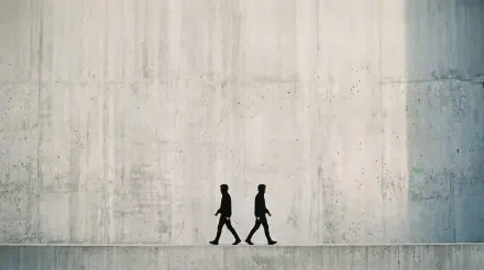 Minimal 5K Ultra HD PC Desktop Wallpaper and Background — two walking silhouettes cross a long, textured concrete wall under soft, neutral light.