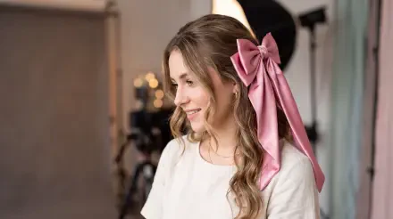 Smiling woman with long wavy hair tied with a large pink bow in a studio setting — 5K Ultra HD PC desktop wallpaper and background.
