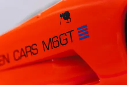 Close-up of bright orange McLaren G6GT vehicle showing the M6GT badge and body detail — 8K Ultra HD PC desktop wallpaper/background.