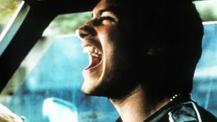 Amores Perros 4K Ultra HD PC desktop wallpaper, close-up of a young man shouting in a car with a tense expression, gritty cinematic grain and teal-tinted lighting.