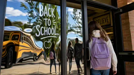 4K Ultra HD PC wallpaper: a student with a purple backpack approaches school doors bearing Back to School lettering, the yellow school bus and reflections visible in the glass.