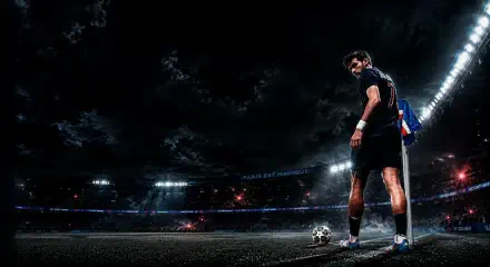 HD PC desktop wallpaper background: dramatic night soccer scene — player by the corner flag with a ball on an illuminated stadium pitch beneath stormy clouds.