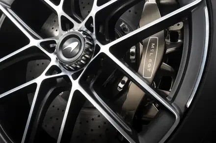 Close-up 8K Ultra HD desktop wallpaper of a McLaren McL 6GT wheel: black multi-spoke rim, McLaren center cap, drilled brake rotor and branded caliper.