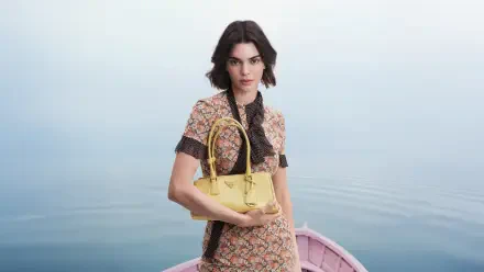 Celebrity fashion model in patterned dress with black tie holding a yellow handbag in a pink rowboat on calm water — 5K Ultra HD PC desktop wallpaper.