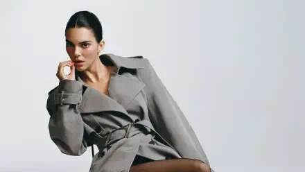 4K Ultra HD desktop wallpaper: celebrity model in a tailored gray trench coat, seated against a pale backdrop, poised with hand near her chin.