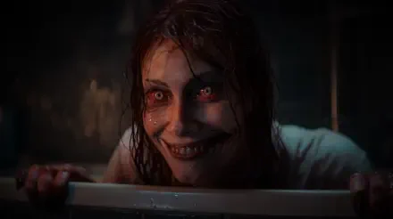 Evil Dead Rise close-up: a possessed deadite woman with bloodshot eyes, torn lips and a manic grin — horror 5K Ultra HD PC desktop wallpaper/background.