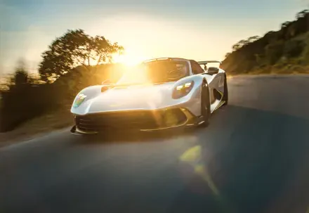 Aston Martin Valhalla Spider sports car speeding along a sunlit road in an 8K Ultra HD PC desktop wallpaper.