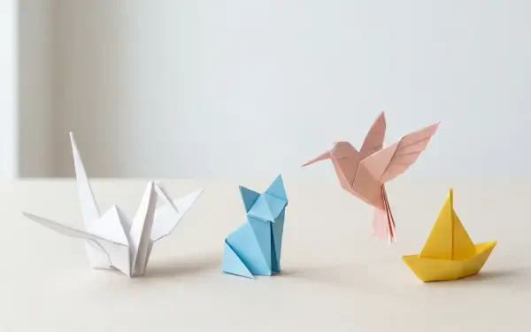 Clean 5K Ultra HD PC desktop wallpaper and background showing a minimal beige surface with four origami figures: white crane, blue folded animal, pink hummingbird, yellow paper boat.
