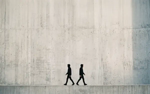 Minimal 5K Ultra HD PC Desktop Wallpaper and Background — two walking silhouettes cross a long, textured concrete wall under soft, neutral light.