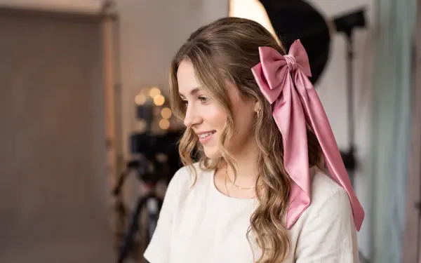 Smiling woman with long wavy hair tied with a large pink bow in a studio setting — 5K Ultra HD PC desktop wallpaper and background.