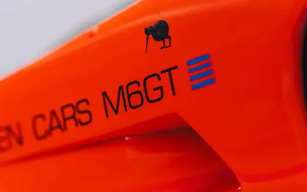Close-up of bright orange McLaren G6GT vehicle showing the M6GT badge and body detail — 8K Ultra HD PC desktop wallpaper/background.