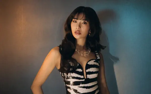 Katseye 4K Ultra HD PC desktop wallpaper: dark-haired woman in a zebra-print dress with layered necklaces, moody teal and amber lighting and a confident pose.