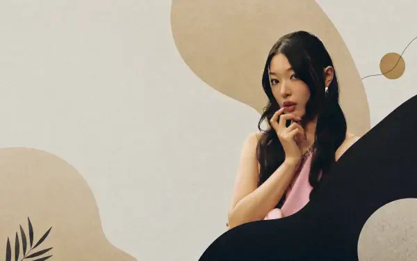Portrait of a woman with long dark hair in a pink top, hand to chin against abstract beige and black shapes — Katseye 4K Ultra HD PC Desktop Wallpaper and Background.