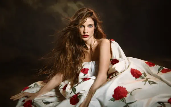 Celebrity model in a white gown patterned with red roses, long wavy hair and red lips reclining against a dark backdrop — 4K Ultra HD PC desktop wallpaper.