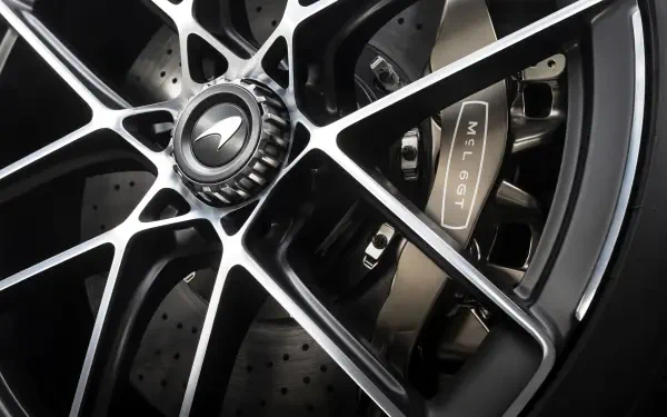 Close-up 8K Ultra HD desktop wallpaper of a McLaren McL 6GT wheel: black multi-spoke rim, McLaren center cap, drilled brake rotor and branded caliper.