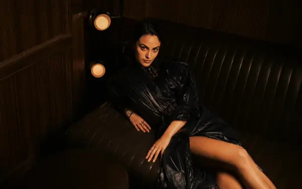 Celebrity actress lounging on a leather sofa in dramatic warm light, wearing a dark evening dress with exposed leg — 4K Ultra HD PC desktop wallpaper/background.