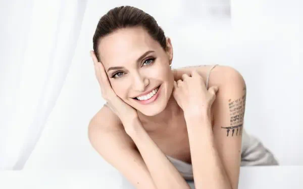 Bright 4K Ultra HD PC desktop wallpaper of a smiling woman reclining, bare-shouldered with an upper-arm tattoo, fresh-faced close-up studio portrait.
