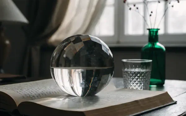 2K Quad HD PC desktop wallpaper: study aesthetic featuring a crystal ball on an open book, a cut-glass tumbler and green bottle on a sunlit desk by a window.