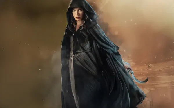 5K Ultra HD PC desktop wallpaper In The Lost Lands: a hooded woman in a dark, flowing cloak strides through a misty, sepia-toned, otherworldly landscape.