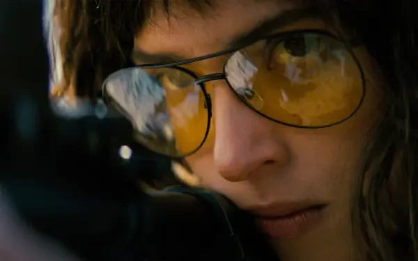 Close-up portrait of a female actor wearing yellow-tinted glasses, intense, focused gaze in a cinematic Onslaught style — 4K Ultra HD PC desktop wallpaper/background.
