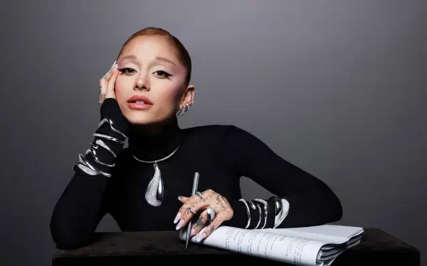 Stylish female pop singer in black turtleneck, bold makeup and statement jewelry, posing with a notebook; 2K Quad HD PC desktop wallpaper evoking music and studio vibes.