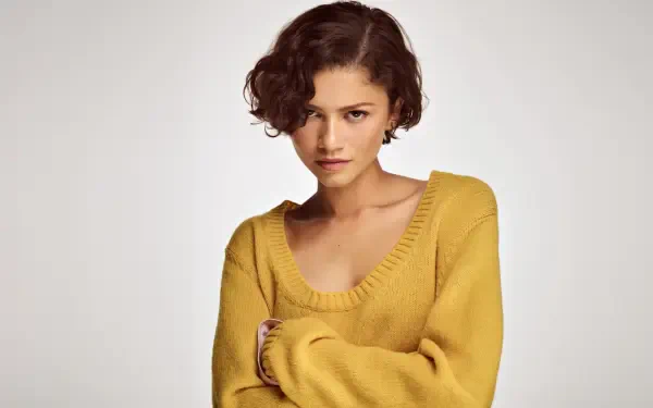 Close-up portrait of a young woman with short curly hair wearing a mustard sweater against a neutral backdrop — 5K Ultra HD PC desktop wallpaper/background.