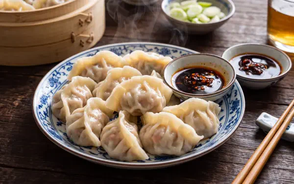 Steamed Chinese dumplings with dipping sauces on a wooden table, 5K Ultra HD PC desktop wallpaper and background.