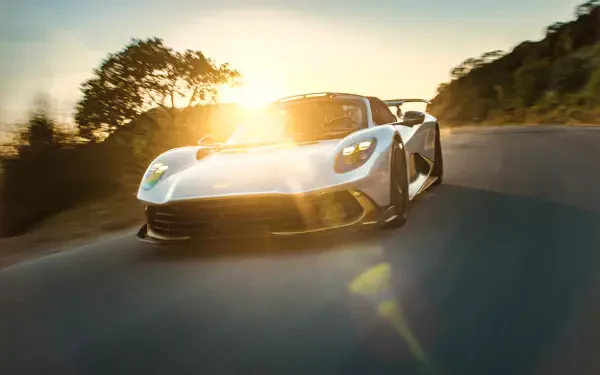 Aston Martin Valhalla Spider sports car speeding along a sunlit road in an 8K Ultra HD PC desktop wallpaper.
