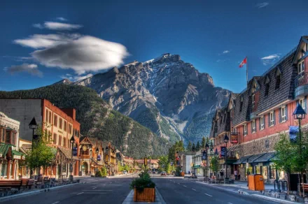 Scenic view of a charming street in Banff, Canada, framed by the majestic Canadian Rockies and vibrant storefronts, captured in stunning HD quality. A picturesque mountain town experience.