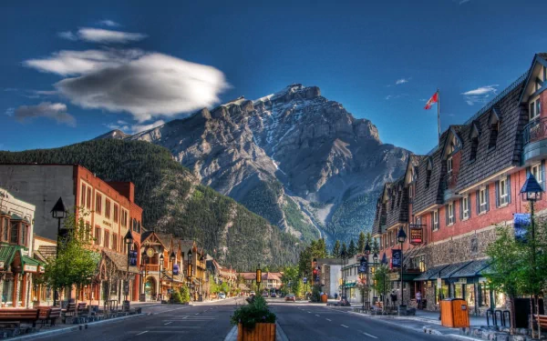 Scenic view of a charming street in Banff, Canada, framed by the majestic Canadian Rockies and vibrant storefronts, captured in stunning HD quality. A picturesque mountain town experience.