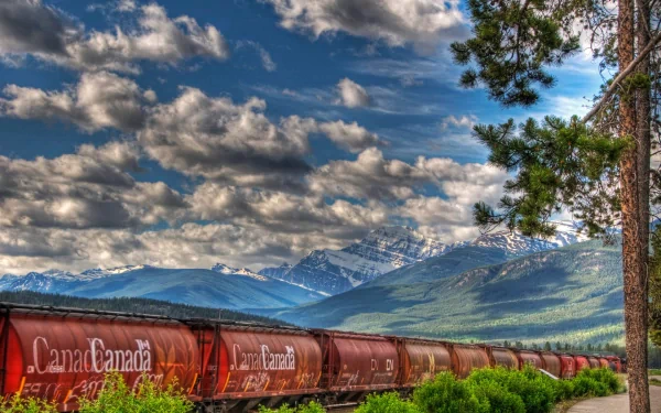 A scenic view of a train in Canada, with vibrant clouds and impressive mountains in the background, creating a stunning HD desktop wallpaper.