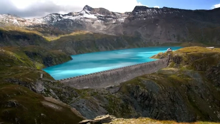 A stunning HD wallpaper showcasing a dam nestled in a breathtaking wilderness landscape, featuring turquoise waters, rocky terrain, and majestic mountains in the background.