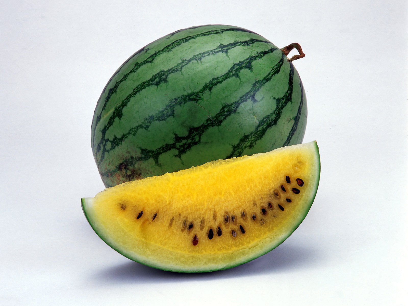 HD PC desktop wallpaper featuring a close-up of a whole watermelon and a slice with yellow flesh and black seeds against a plain background.