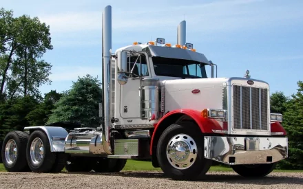 HD PC desktop wallpaper featuring a classic Peterbilt truck parked on a gravel surface with trees and a clear sky in the background.