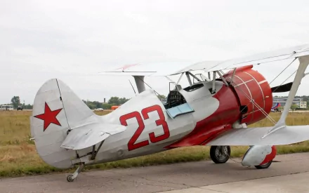 HD desktop wallpaper featuring a vintage red and white biplane aircraft with the number 23 on its side, parked on a runway with a cloudy sky background.