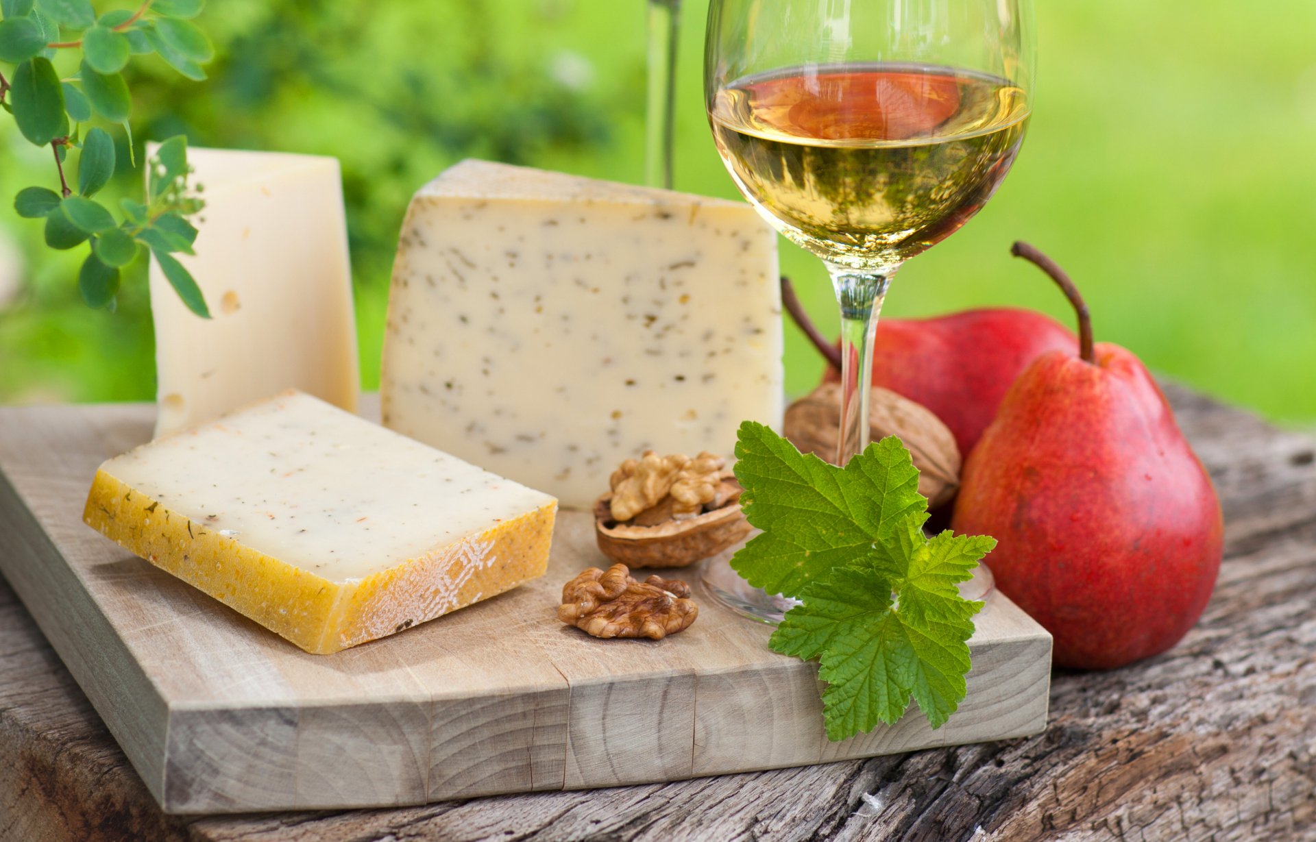 A 4K Ultra HD desktop wallpaper featuring assorted cheeses, walnuts, a glass of white wine, and pears on a rustic wooden board with a blurred green background.
