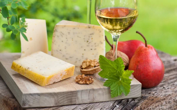 A 4K Ultra HD desktop wallpaper featuring assorted cheeses, walnuts, a glass of white wine, and pears on a rustic wooden board with a blurred green background.