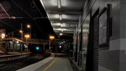 HD PC desktop wallpaper and background: nighttime man-made railroad station platform lit by fluorescent lights, curved tracks vanishing into a dark tunnel, empty sheltered waiting area.