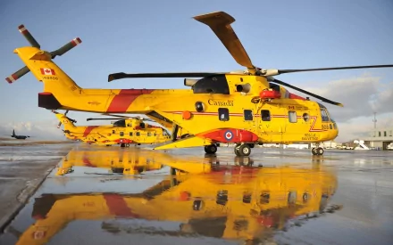 A vibrant AgustaWestland CH-149 Cormorant helicopter in striking yellow reflects on a wet tarmac in Canada, showcasing its impressive design and capabilities.