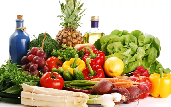 A vibrant arrangement of fresh vegetables and fruits, including peppers, grapes, and leafy greens, complemented by olive oil and a pineapple, creating a colorful and appetizing desktop background.