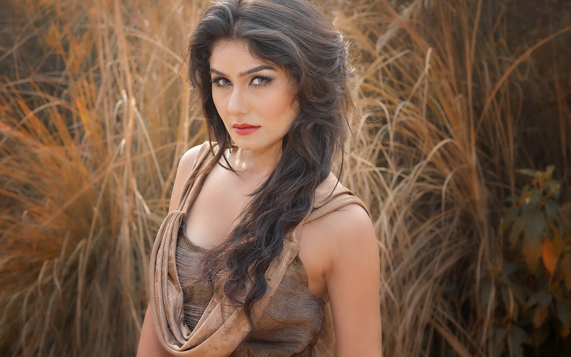 A confident woman model poses against a backdrop of golden grasses, showcasing her striking features in this HD desktop wallpaper.