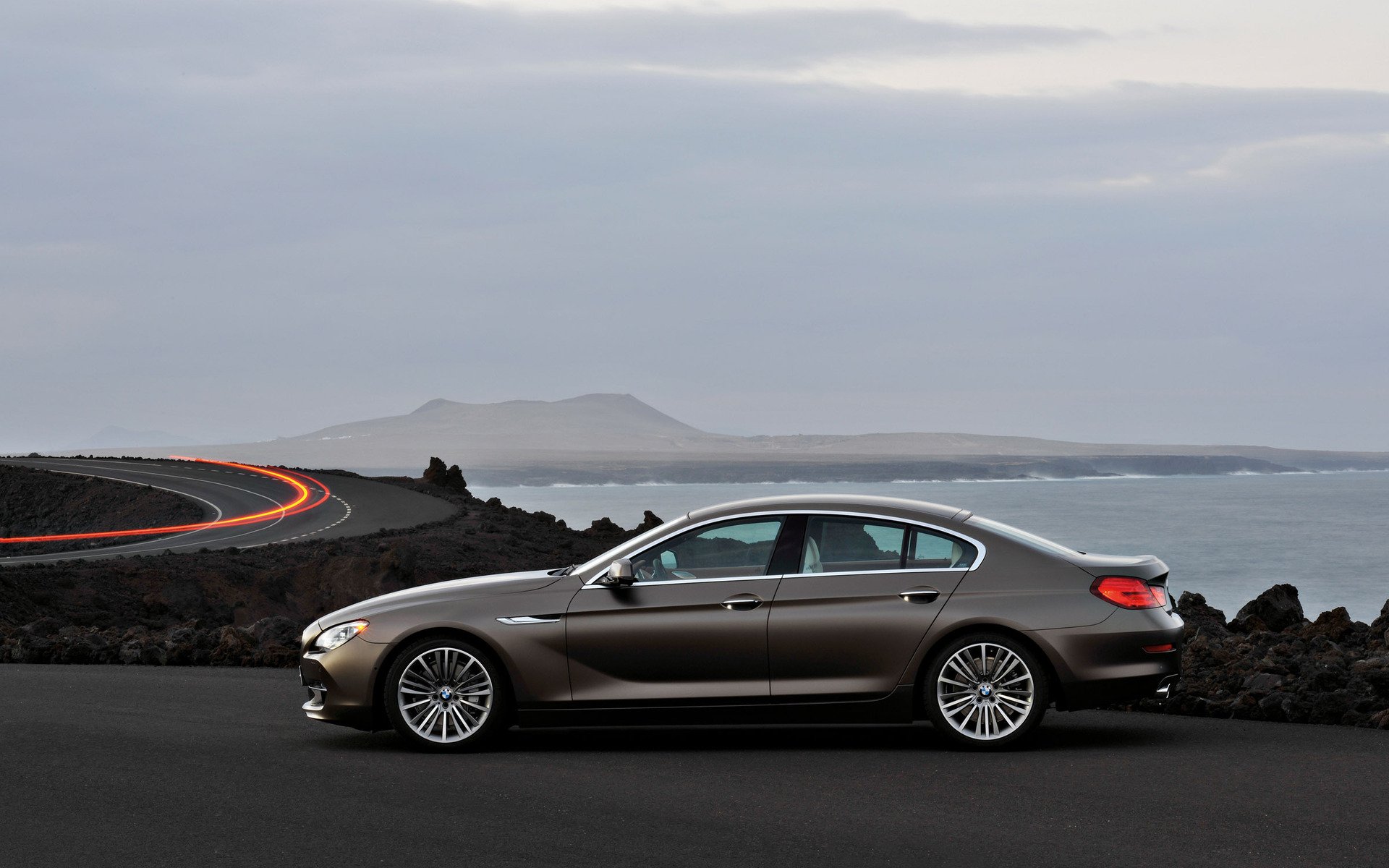 2012 BMW 6 Series Gran Coupe side profile on a coastal road at dusk — HD PC desktop wallpaper with ocean and distant headlands.