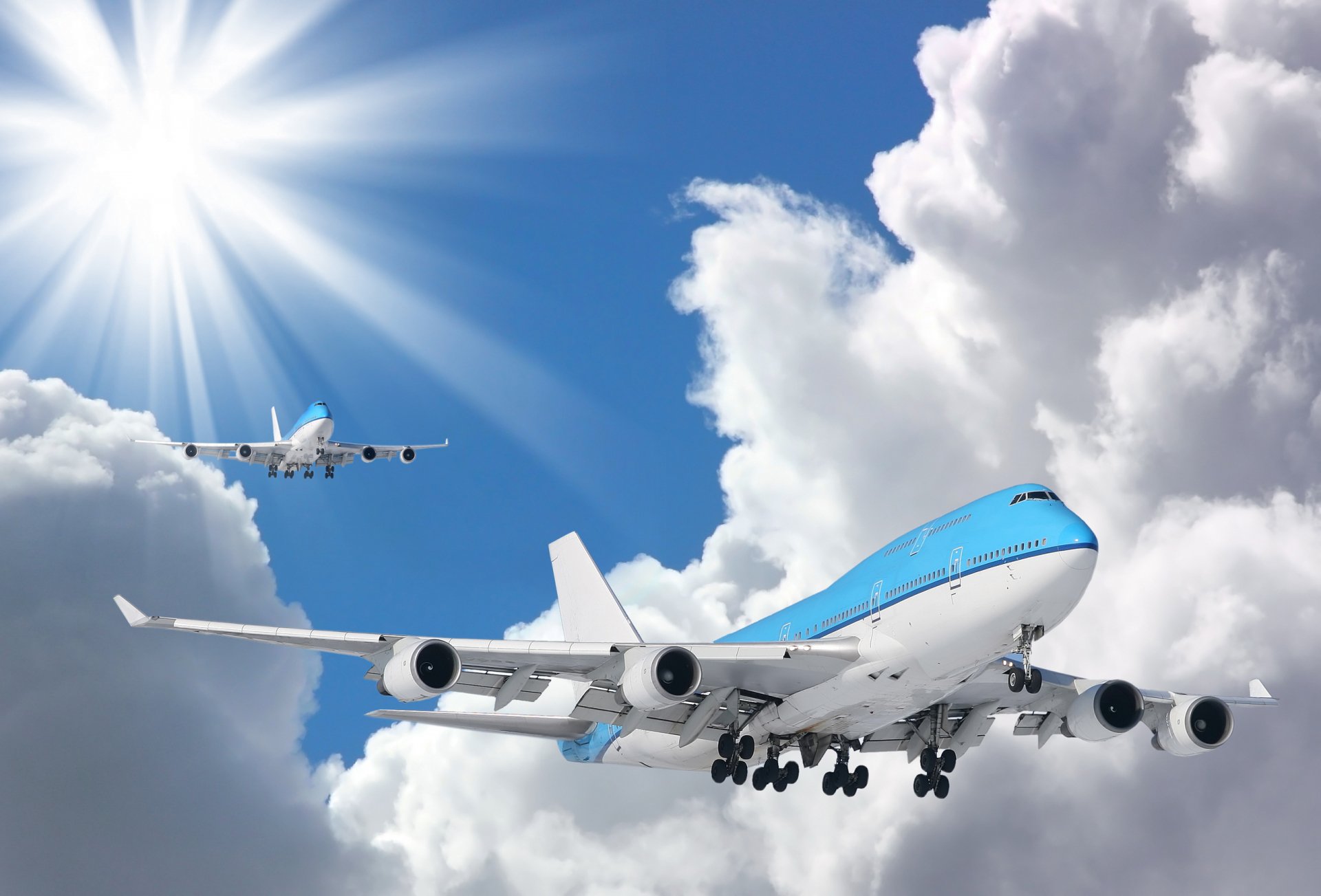HD PC desktop wallpaper of two aircraft flying through bright, partly cloudy skies with sunlight streaming in the background.