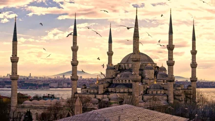 A stunning HD image of the Sultan Ahmed Mosque at sunset, showcasing its majestic minarets and rich architectural details, set against a vibrant sky and city backdrop.